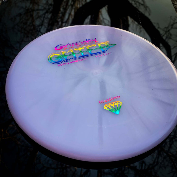 A lavender Gateway Chief - Diamond putter with a beaded rim, iridescent lettering, and a diamond logo sits on a reflective dark surface with tree branches in the background.