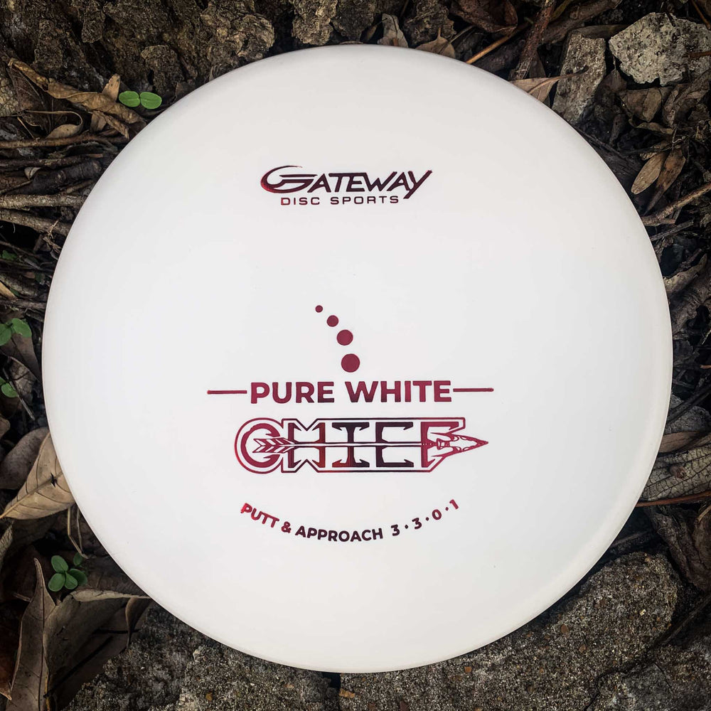 A Chief - Pure White disc golf putter with a beaded rim, ideal for Putt & Approach shots and extra control, lies on the ground among dry leaves and rocks.