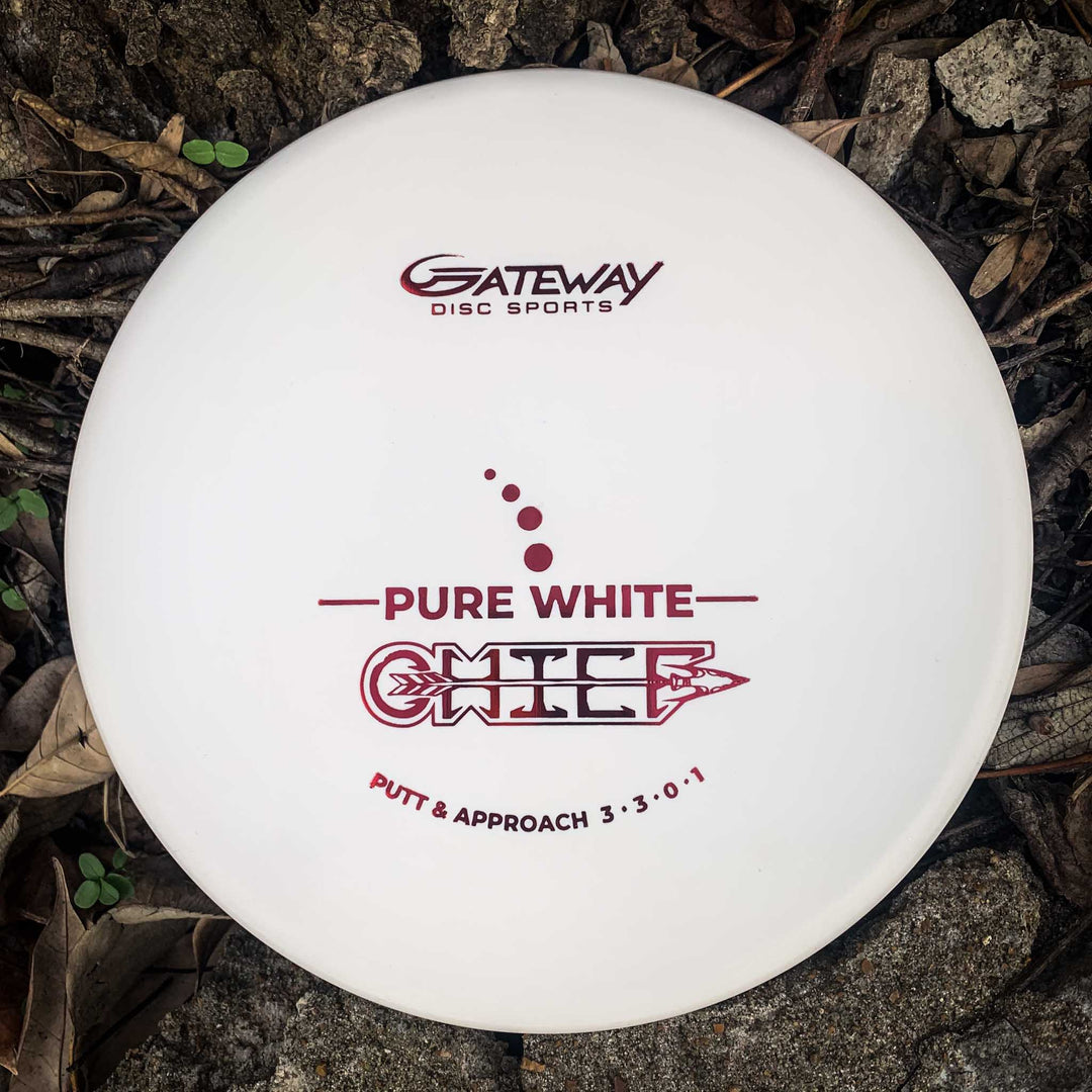 A Chief - Pure White disc golf putter with a beaded rim, ideal for Putt & Approach shots and extra control, lies on the ground among dry leaves and rocks.