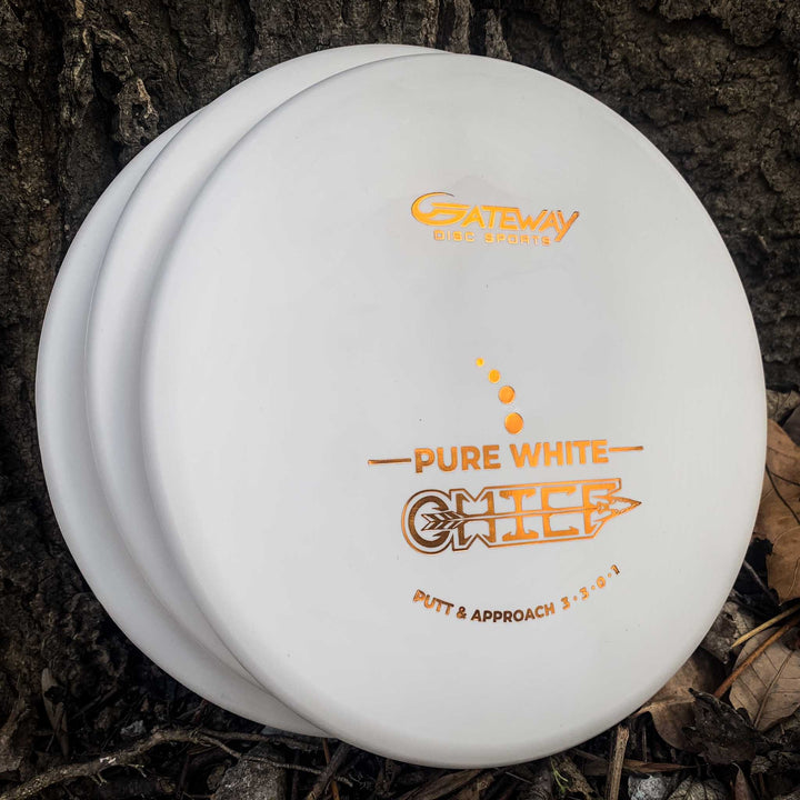 Three Chief - Pure White discs with a beaded rim lean against a tree trunk, surrounded by dried leaves and dirt—ideal for Putt & Approach shots that demand extra control.