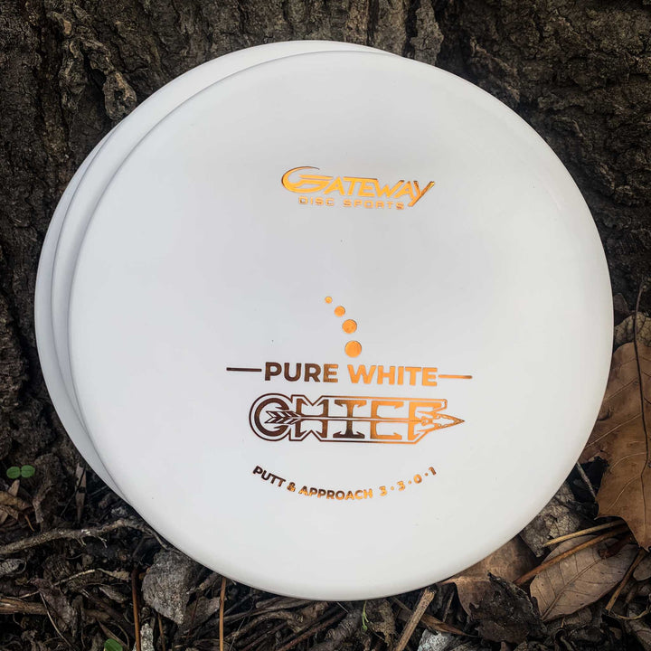 A Chief - Pure White golf disc by Gateway Disc Sports, featuring a beaded rim for extra control, rests against a tree trunk on the ground amidst dry leaves.