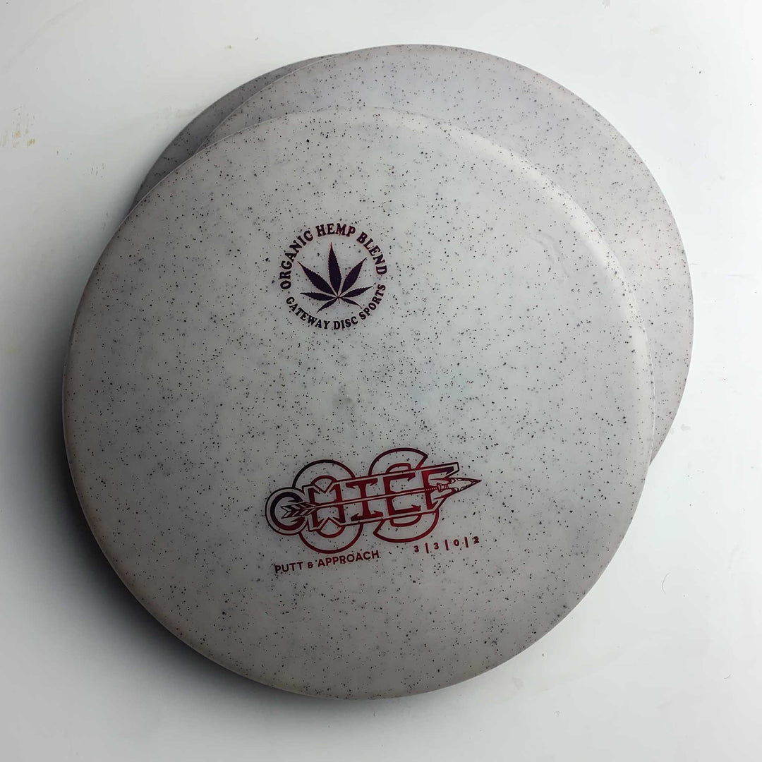 Two white speckled Chief OS - Diamond Hemp disc golf putters are stacked on a white surface; ideal for forehand drives and maintaining a consistent hyzer line with this overstable putter.