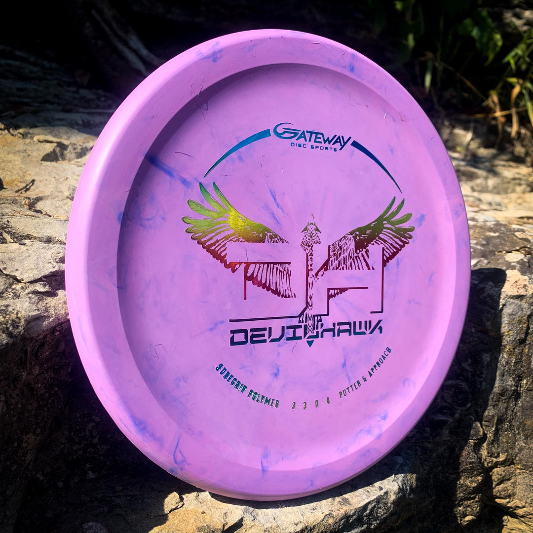 A purple Devilhawk - SureGrip over-stable putter featuring a colorful eagle design and the text "Devilhawk" and "Gateway Disc Sports," shown resting on a rock outdoors.