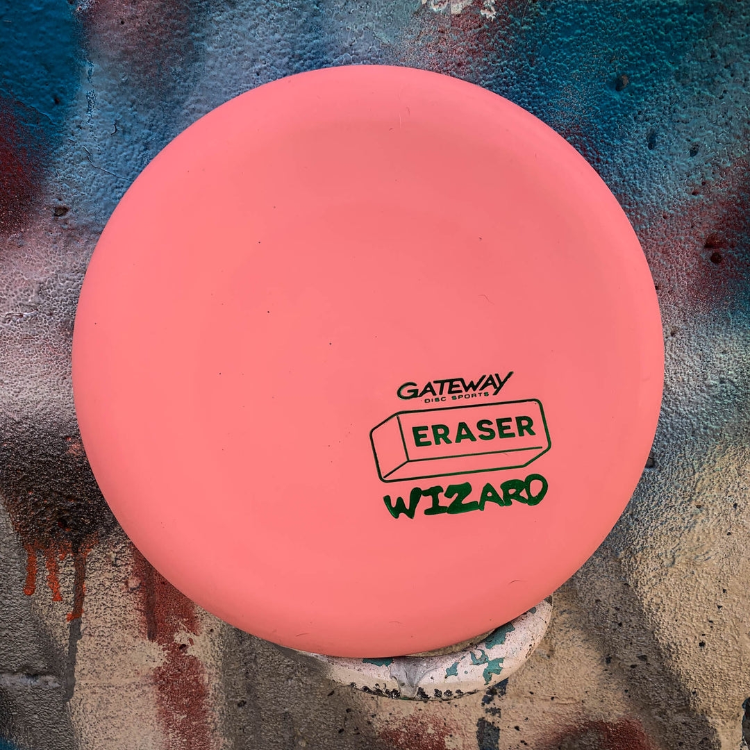 The pink Gateway Wizard - Eraser putter rests by a spray-painted wall—ideal for putts and mid-range drives, even in windy conditions.