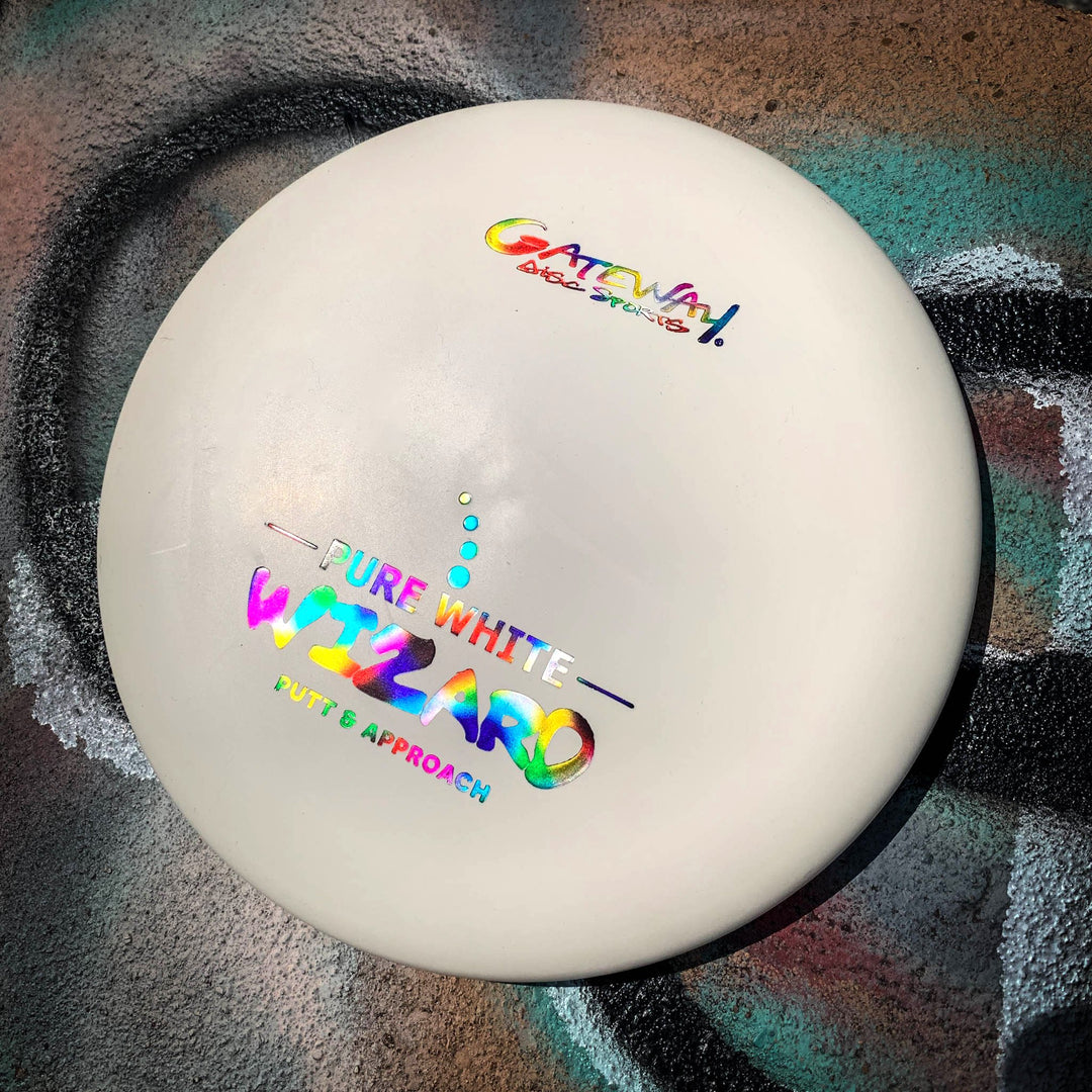 The white "Wizard - Pure White" putter sits on concrete with vibrant graffiti, showcasing its stability and reliability—even in windy conditions.