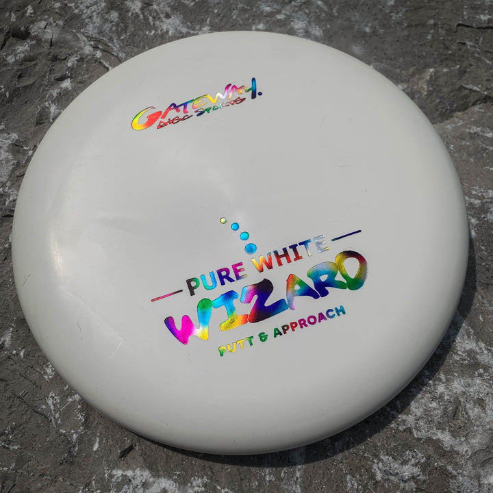 A white Gateway Wizard - Pure White putter with rainbow text rests on gray stone—a reliable choice for confident putting, even in windy conditions.