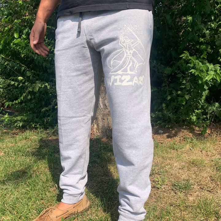 A person standing on grass wears Gateway Joggers in light gray, featuring a Wizard logo and "WIZARD" printed on the left leg. Shrubs and a tree are visible in the background.