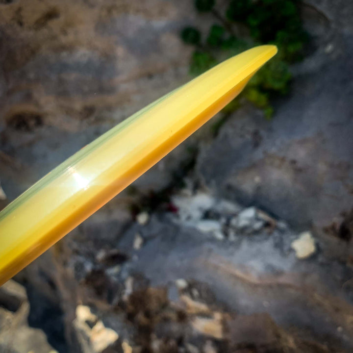 A close-up of the yellow Journey - Diamond long-range distance driver held above a blurred, rocky outdoor background with green vegetation visible.
