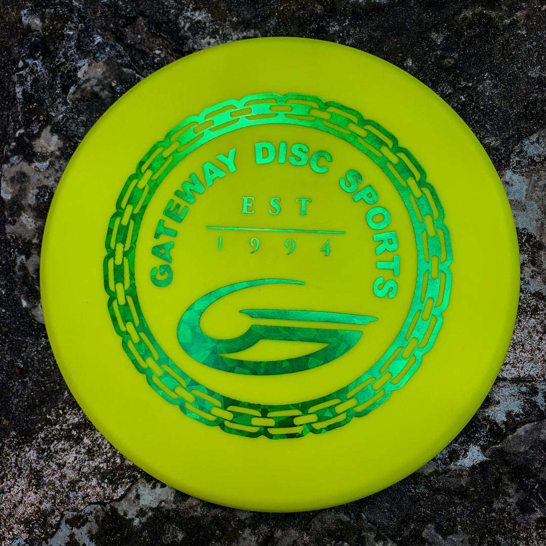 A yellow Lil Wizard - SureGrip™ : 6-1/2" disc with a green "Gateway Disc Sports" logo, est. 1994, rests on a rough stone surface.