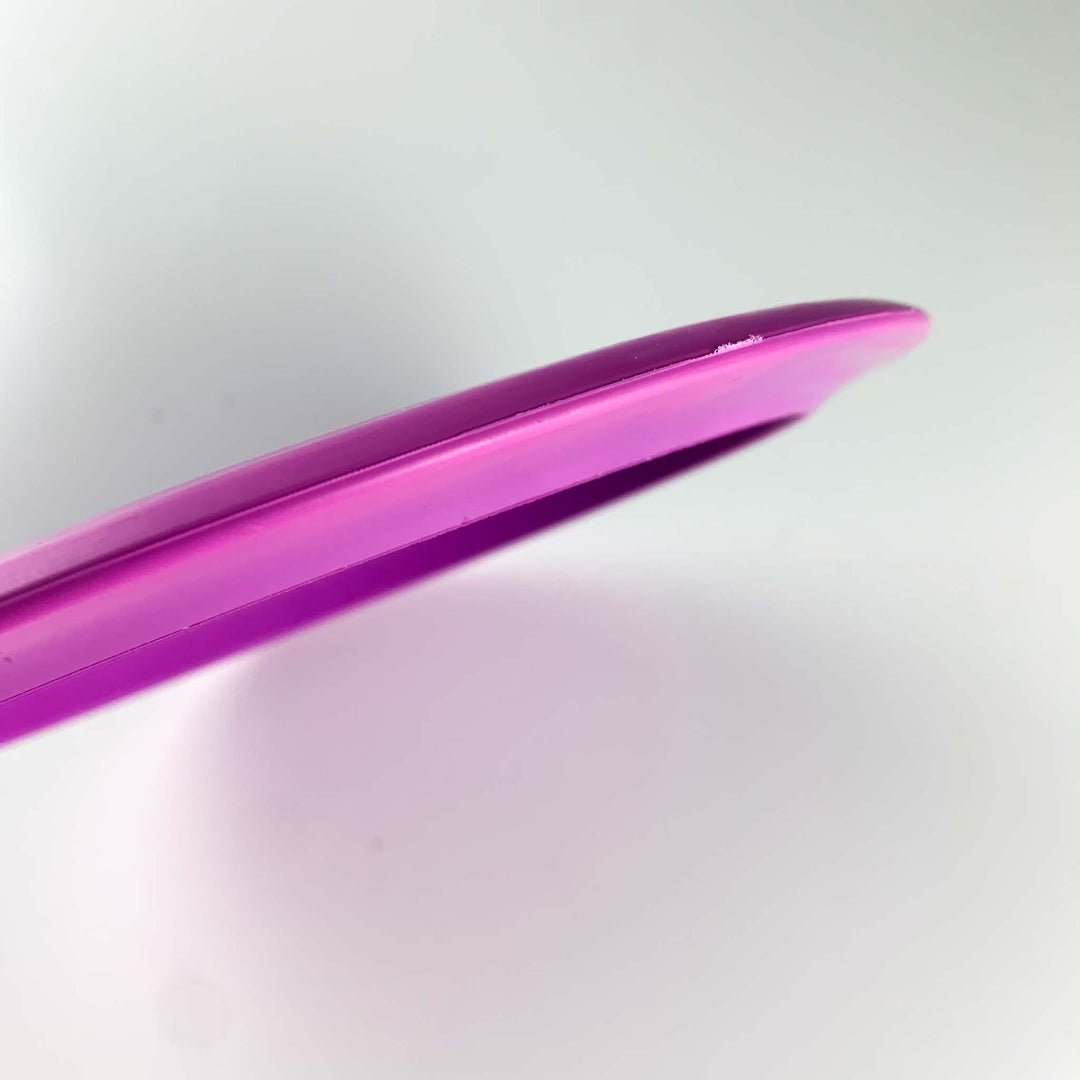 Close-up of the edge of a bright pink Journey Lightweight - SureGrip disc, a long-range distance driver, against a plain white background.