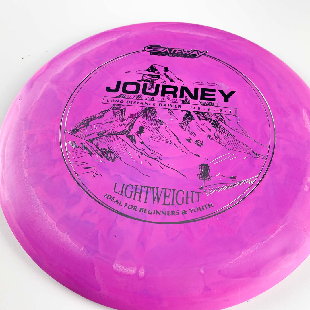 The Journey Lightweight - SureGrip is a pink long-range distance driver by Gateway Disc Sports, with black mountain graphics, offering lightweight, controllable flights—ideal for beginners and youth seeking maximum throw distance.