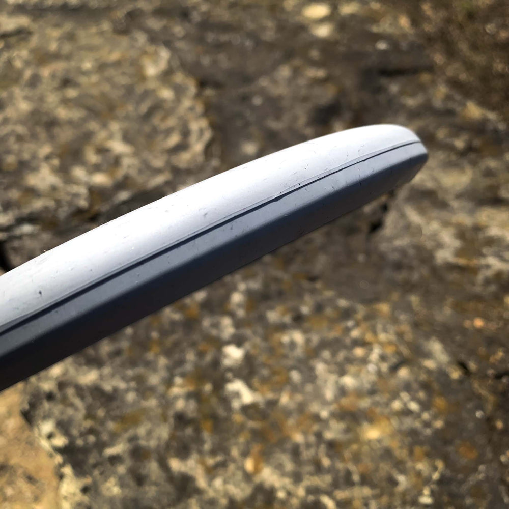 Close-up of the rim and edge of the Magic - Lunar disc golf disc, known for its straight-flying glide, held above rocky ground.