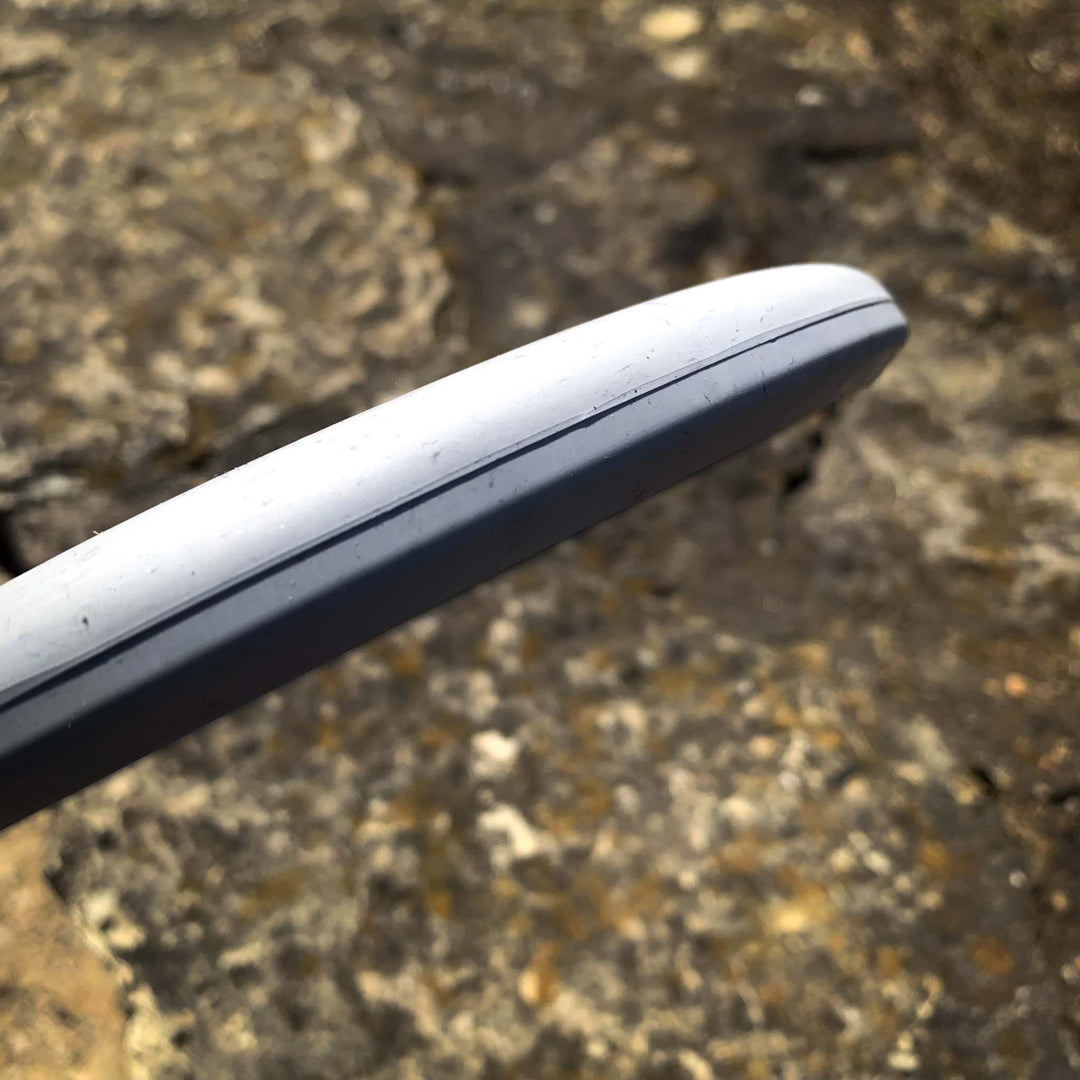 Close-up of the rim and edge of the Magic - Lunar disc golf disc, known for its straight-flying glide, held above rocky ground.