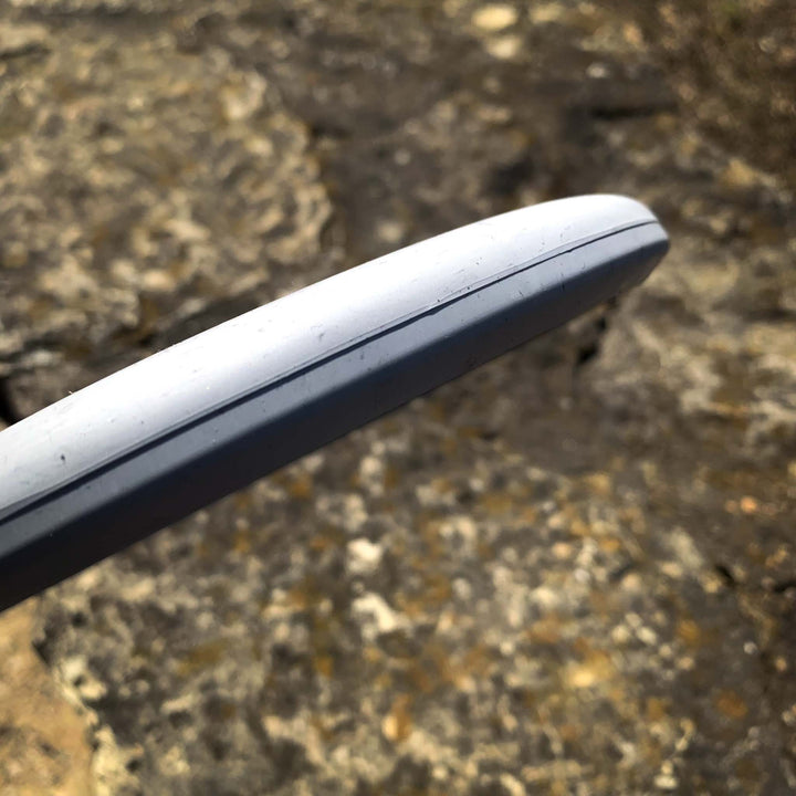 Close-up of the rim and edge of the Magic - Lunar disc golf disc, known for its straight-flying glide, held above rocky ground.