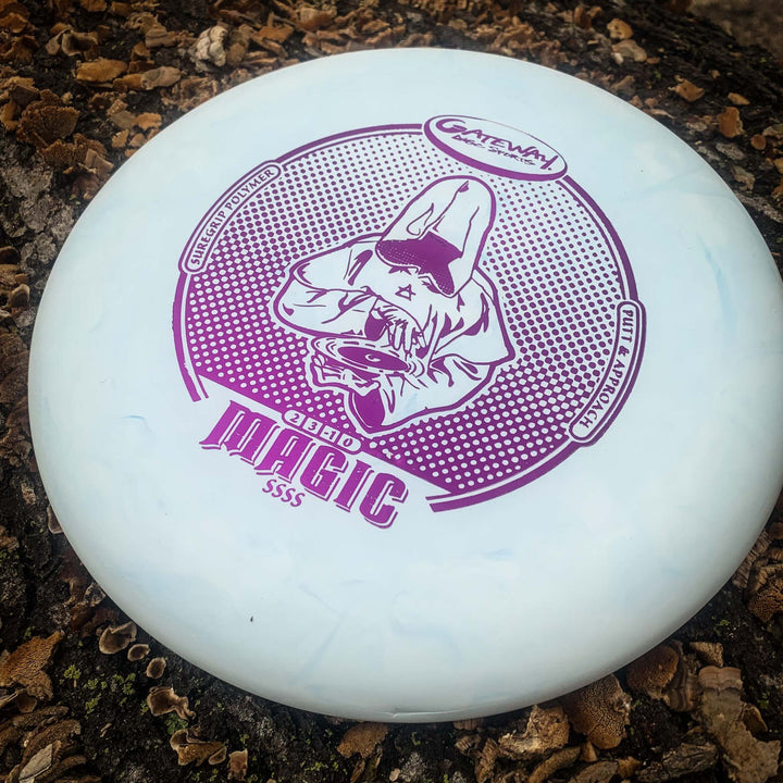A light blue disc golf putter, the Magic - Suregrip - SSSS, featuring a purple hooded figure and "Gateway Disc Sports" text, rests on a rough textured surface.