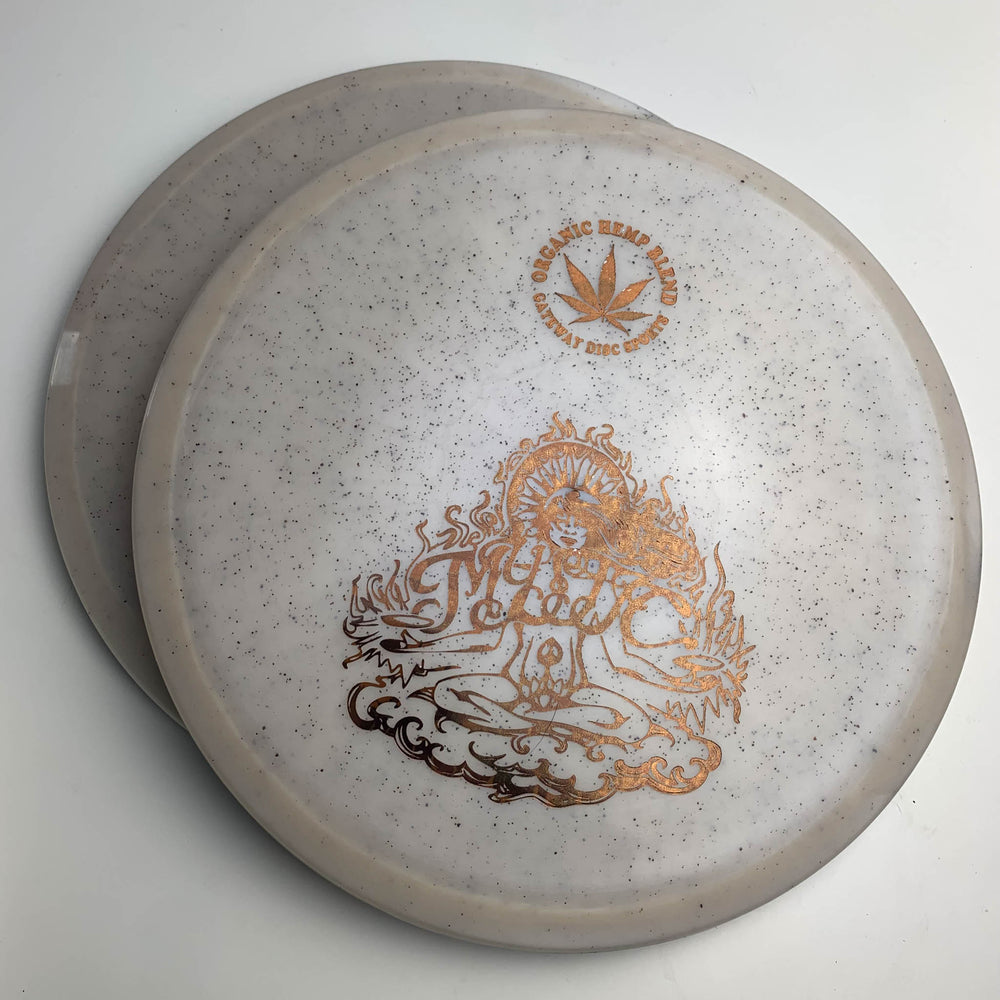 The Mystic - Diamond Hemp features two white speckled discs with gold designs—one with a hemp leaf and "100% Organic Hemp Blend" text, the other with a meditative figure in flames. Enjoy controllable mid-range, straight flights, and great glide.
