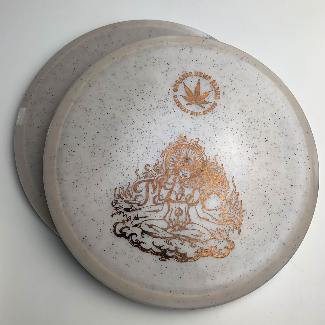 The Mystic - Diamond Hemp features two white speckled discs with gold designs—one with a hemp leaf and "100% Organic Hemp Blend" text, the other with a meditative figure in flames. Enjoy controllable mid-range, straight flights, and great glide.