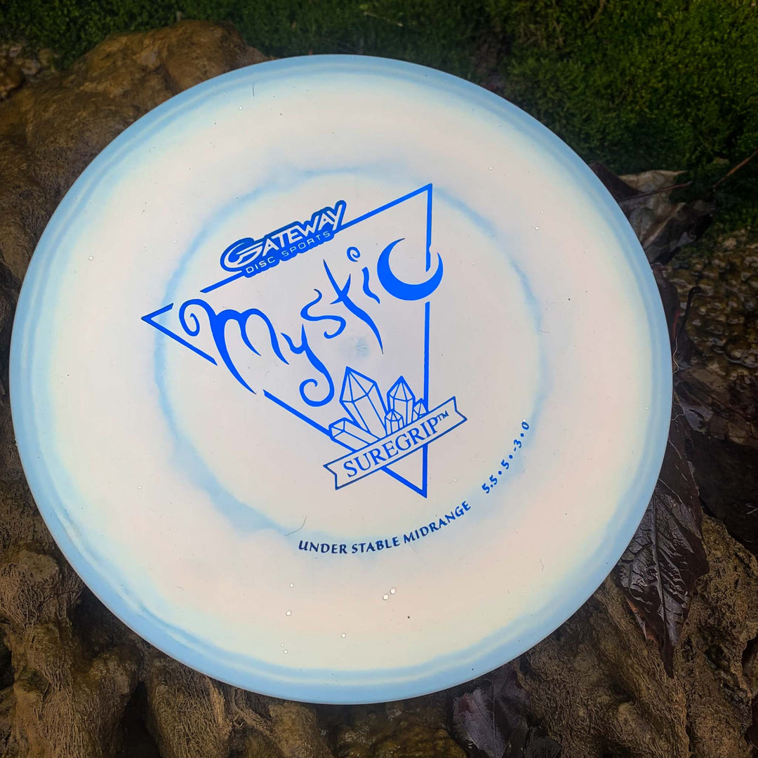 A light blue Mystic - SureGrip disc from Gateway Disc Sports with crystal graphics rests on a rock, celebrated for its controllable mid-range flight and impressive glide.