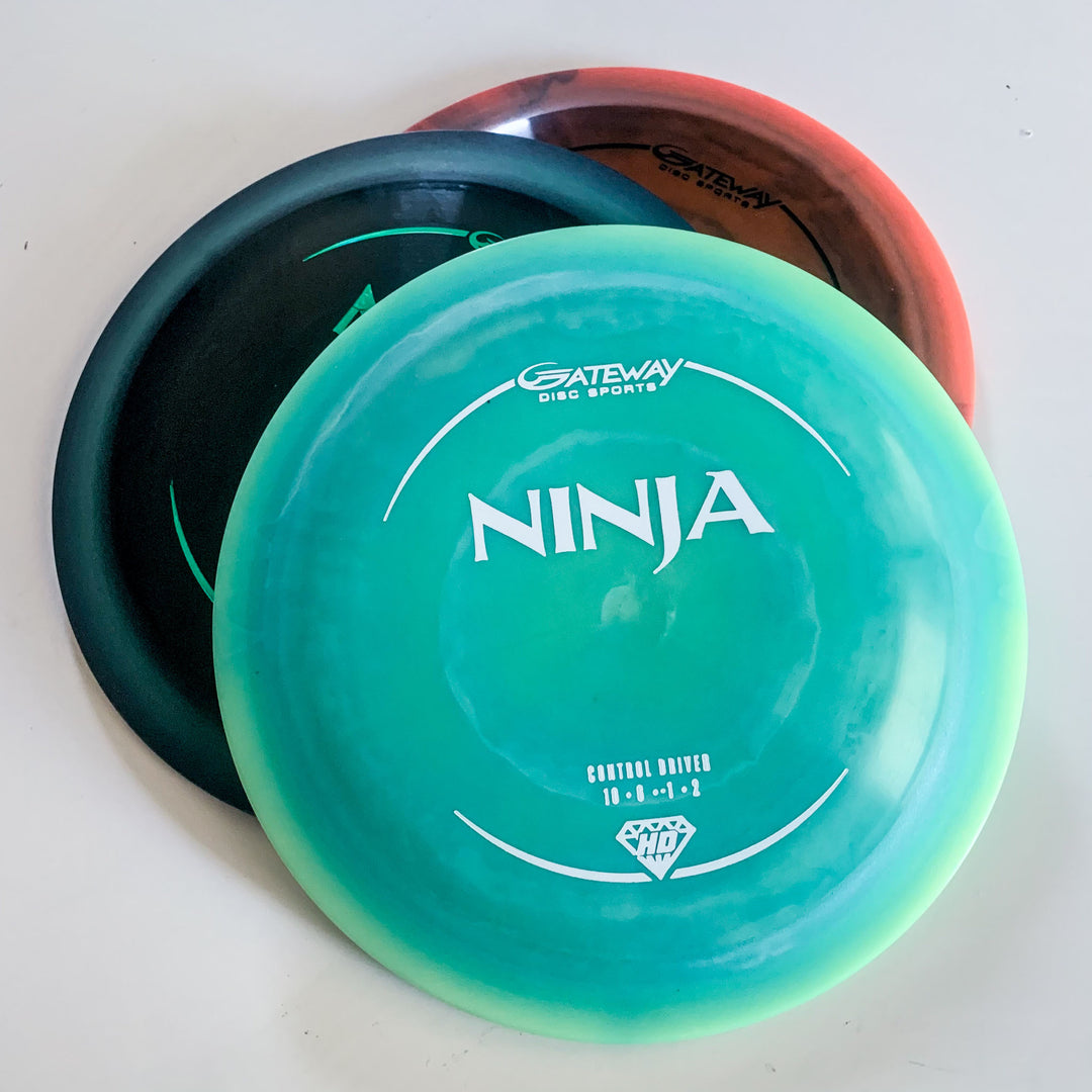 Three stacked disc golf discs, with the top labeled —Ninja - (HD) Hyper Diamond—� by Gateway Disc Sports, featuring HD Ninja drag reducing surface technology in green and blue shades on a white background.