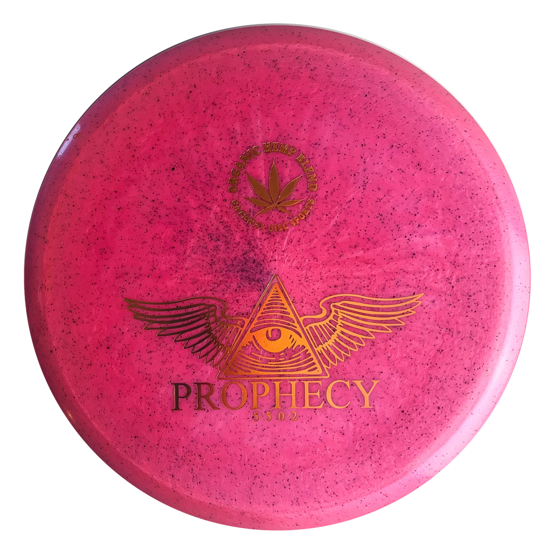 The Prophecy - Diamond Hemp is a pink, overstable mid-range disc golf disc with a speckled pattern, featuring a winged eye in a triangle and "PROPHECY" in gold on the front. Made from premium Diamond blend hemp plastic for consistent flight.