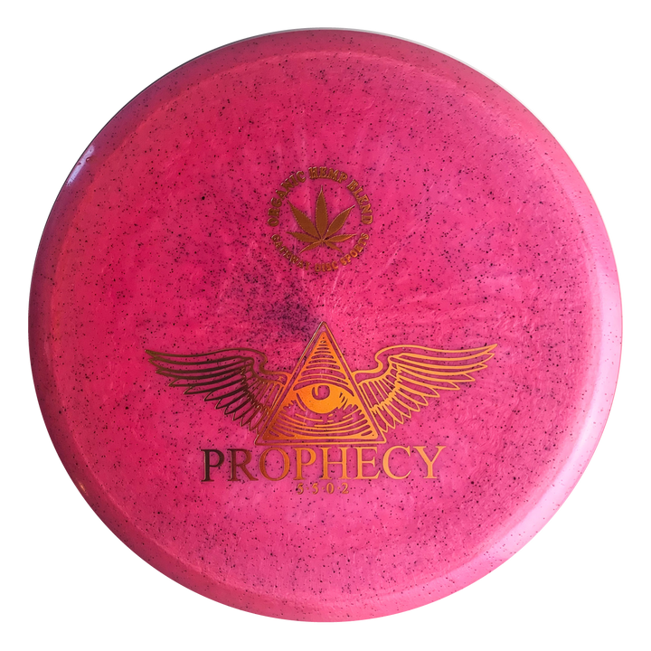 The Prophecy - Diamond Hemp is a pink, overstable mid-range disc golf disc with a speckled pattern, featuring a winged eye in a triangle and "PROPHECY" in gold on the front. Made from premium Diamond blend hemp plastic for consistent flight.
