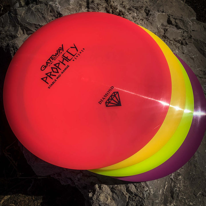 A stack of colorful discs sits on a rock, with the top labeled "Prophecy - Diamond," featuring a premium Diamond blend for reliable flight.