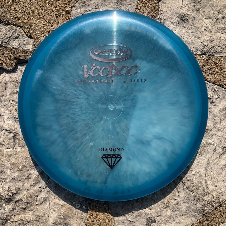 A blue Voodoo - Diamond putter from Latitude 64 rests on a textured stone surface, viewed from above.