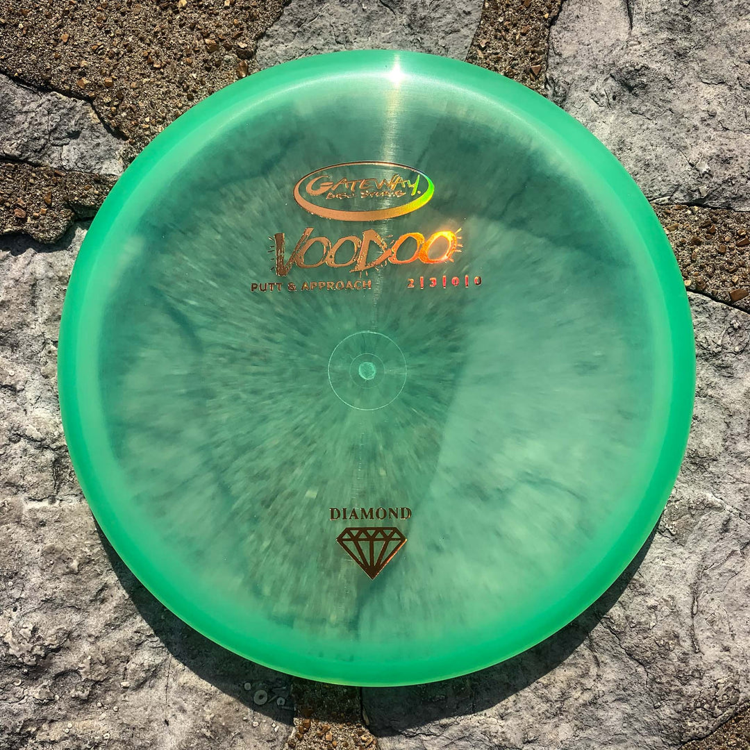 A Voodoo - Diamond putter in green rests on a stone surface under direct sunlight, providing reliable performance and a comfortable hand feel.