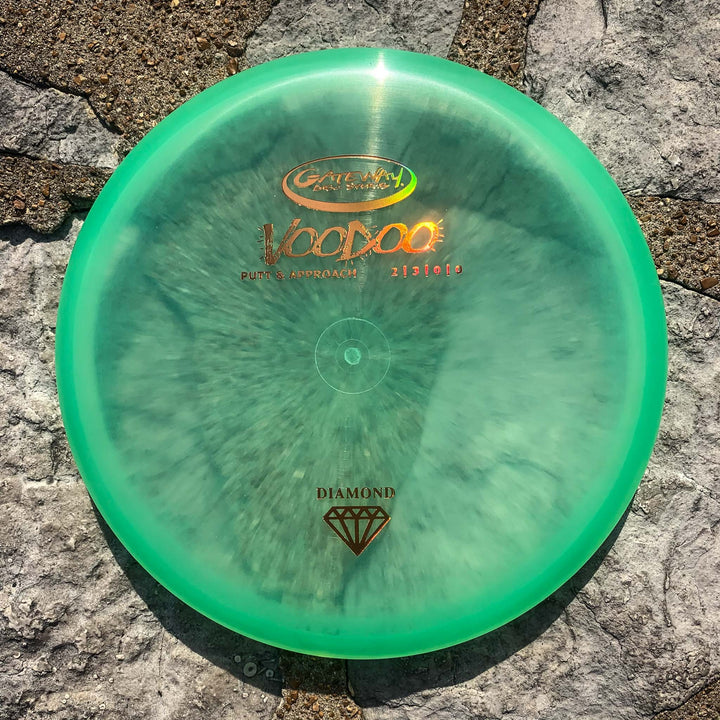 A Voodoo - Diamond putter in green rests on a stone surface under direct sunlight, providing reliable performance and a comfortable hand feel.