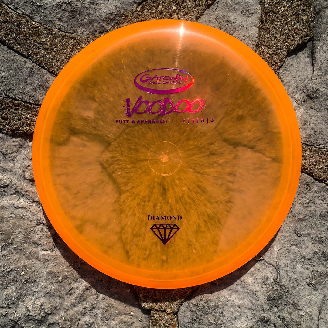 A Voodoo - Diamond putter, known for its straight-line accuracy and comfortable grip, sits on gray stone pavement under direct sunlight.