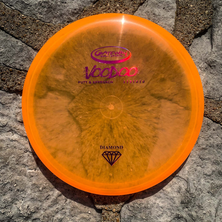 A Voodoo - Diamond putter, known for its straight-line accuracy and comfortable grip, sits on gray stone pavement under direct sunlight.