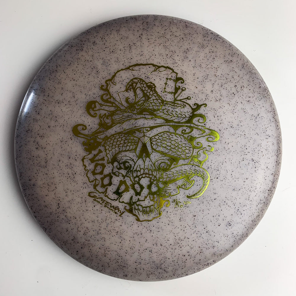 A speckled gray Voodoo - Diamond Hemp putter disc golf disc featuring a gold line art design of a snake coiled around a skull.