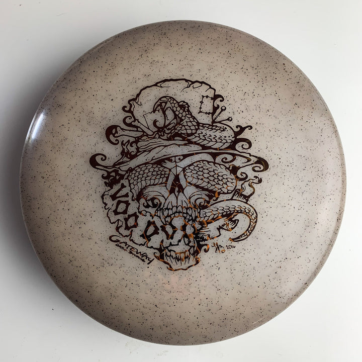 A tan Voodoo - Diamond Hemp putter disc golf disc featuring a detailed black illustration of a snake coiled around a top-hat-wearing skull.