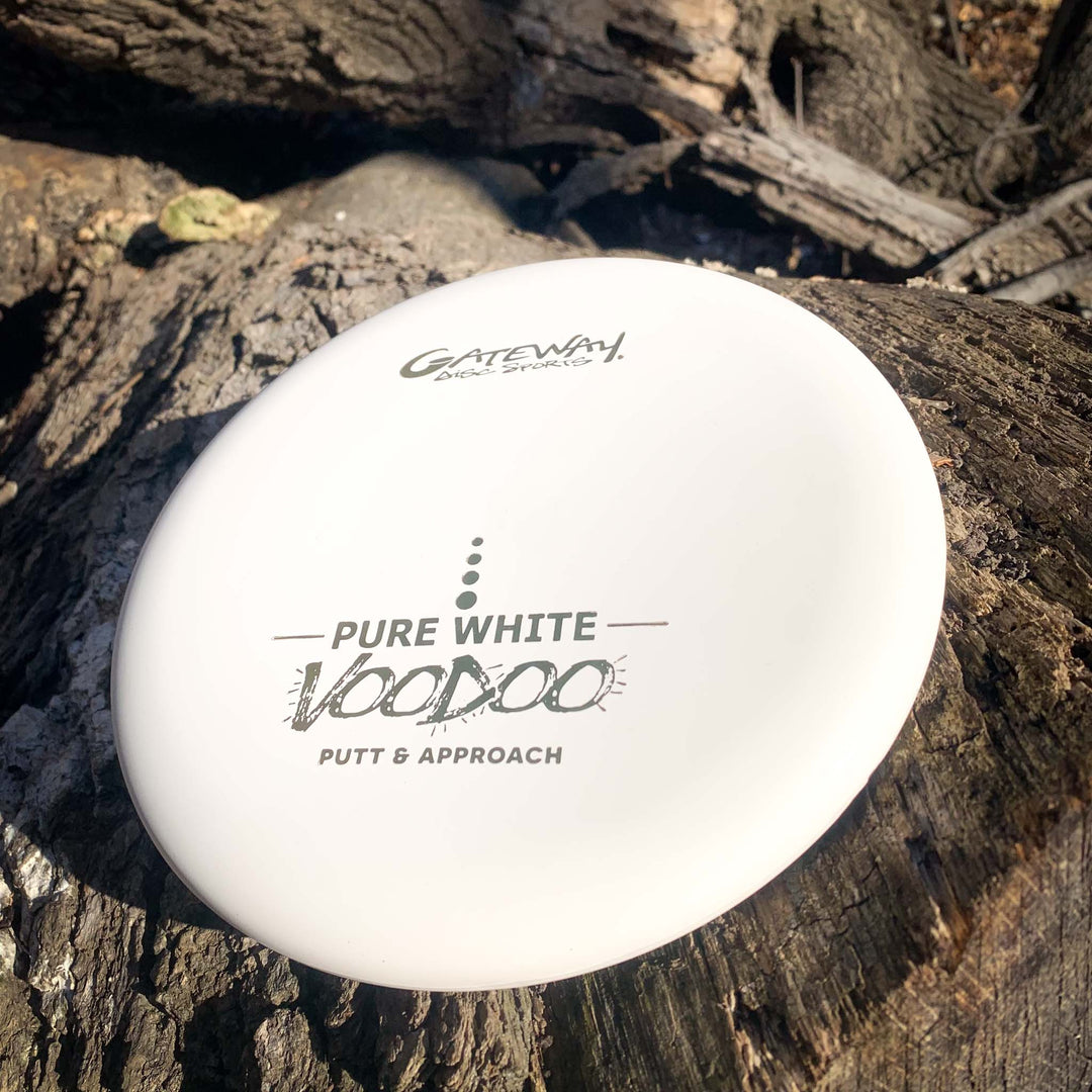 A white Voodoo - Pure White putter rests on a tree trunk outdoors.