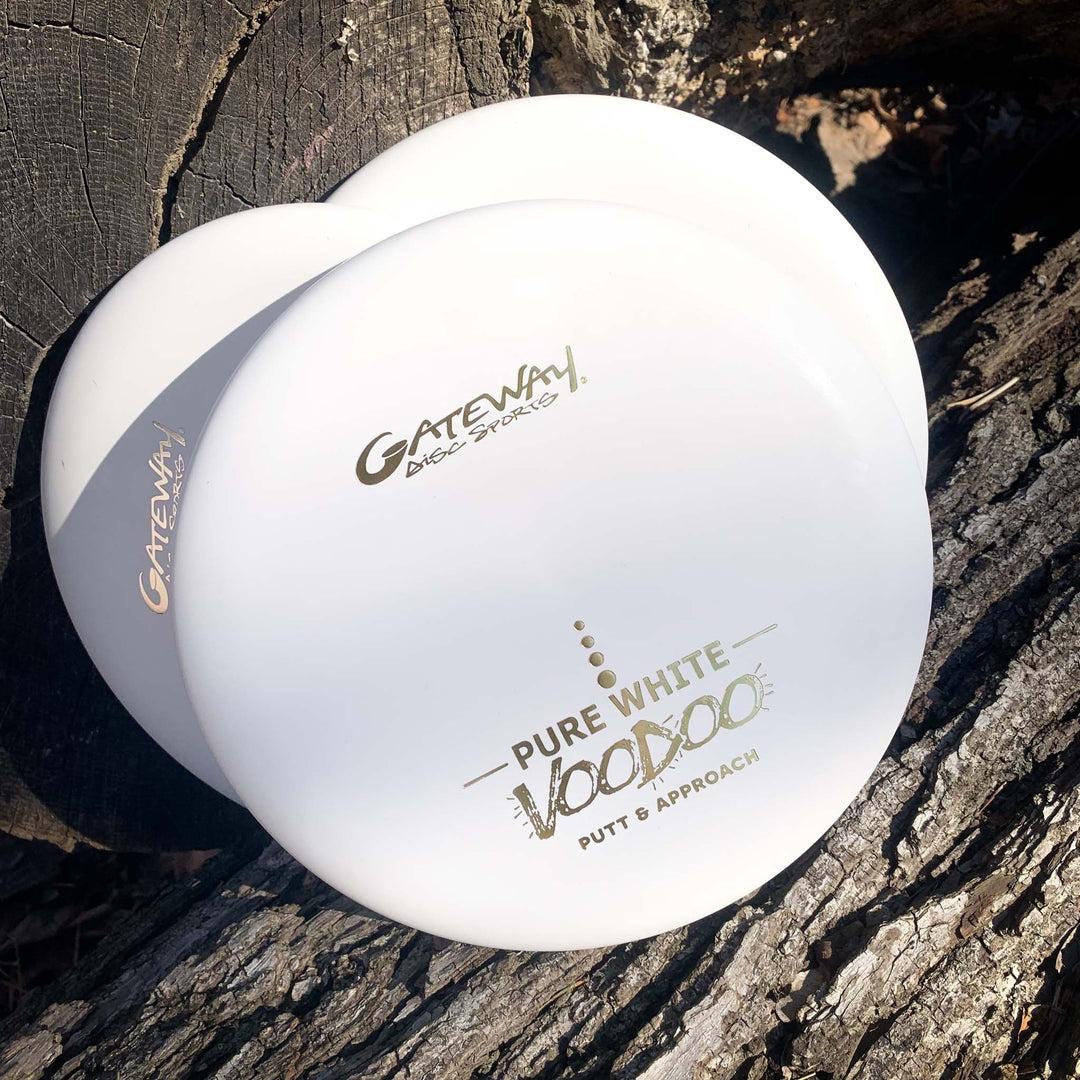Two white Gateway Voodoo - Pure White putters rest on rough tree bark in sunlight, ideal for fans of the Voodoo or Wizard series.