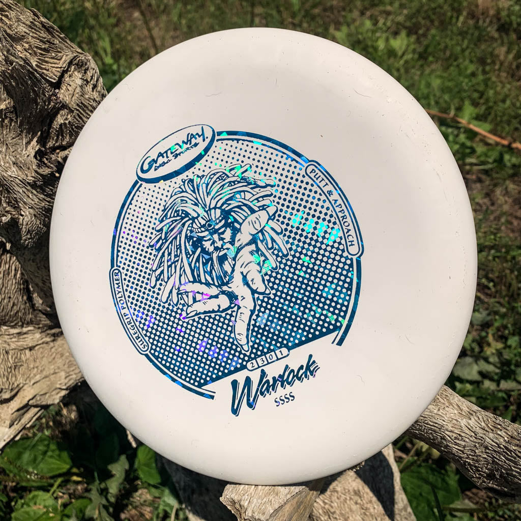 A white Warlock - Suregrip - SSSS putter with blue graphics and text sits on a tree branch, ideal for sharpening your approach shots among lush green grass.
