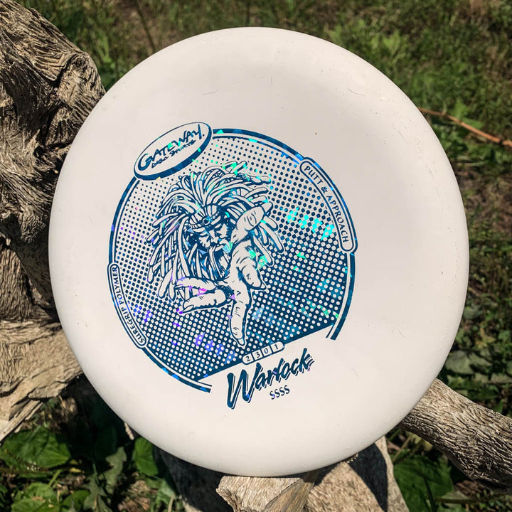 A white Warlock - Suregrip - SSSS putter with blue graphics and text sits on a tree branch, ideal for sharpening your approach shots among lush green grass.