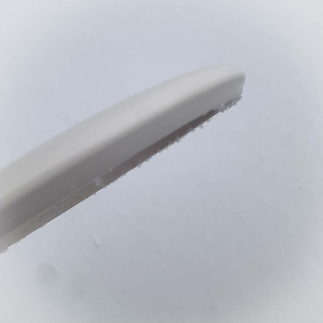 Close-up of the Warlock - Pure White ice scraper with frost on its edge, set against a pale background—ready to tackle winter's chill with ease.