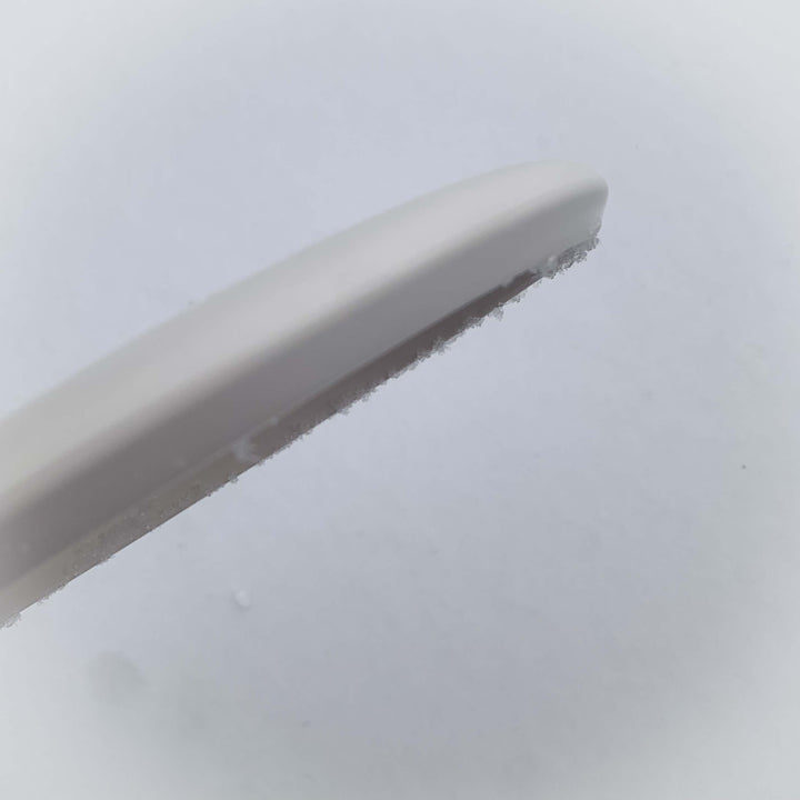 Close-up of the Warlock - Pure White ice scraper with frost on its edge, set against a pale background—ready to tackle winter's chill with ease.