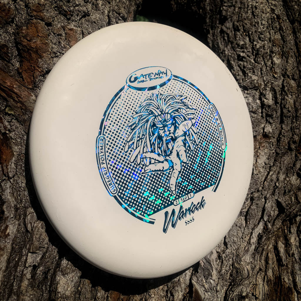 A white Warlock - Suregrip - SSSS disc golf putter with a blue holographic design leans against tree bark, ready to elevate your approach game.