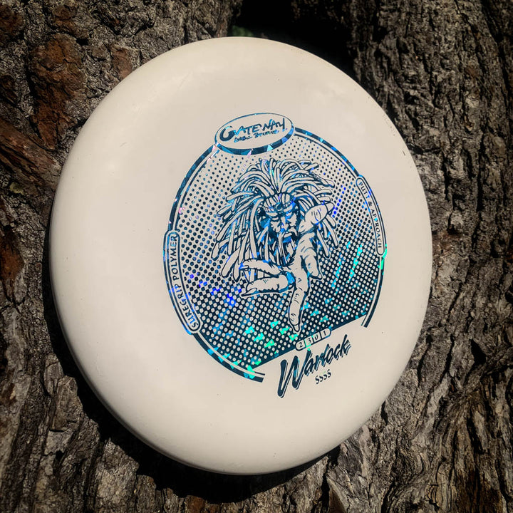 A white Warlock - Suregrip - SSSS disc golf putter with a blue holographic design leans against tree bark, ready to elevate your approach game.