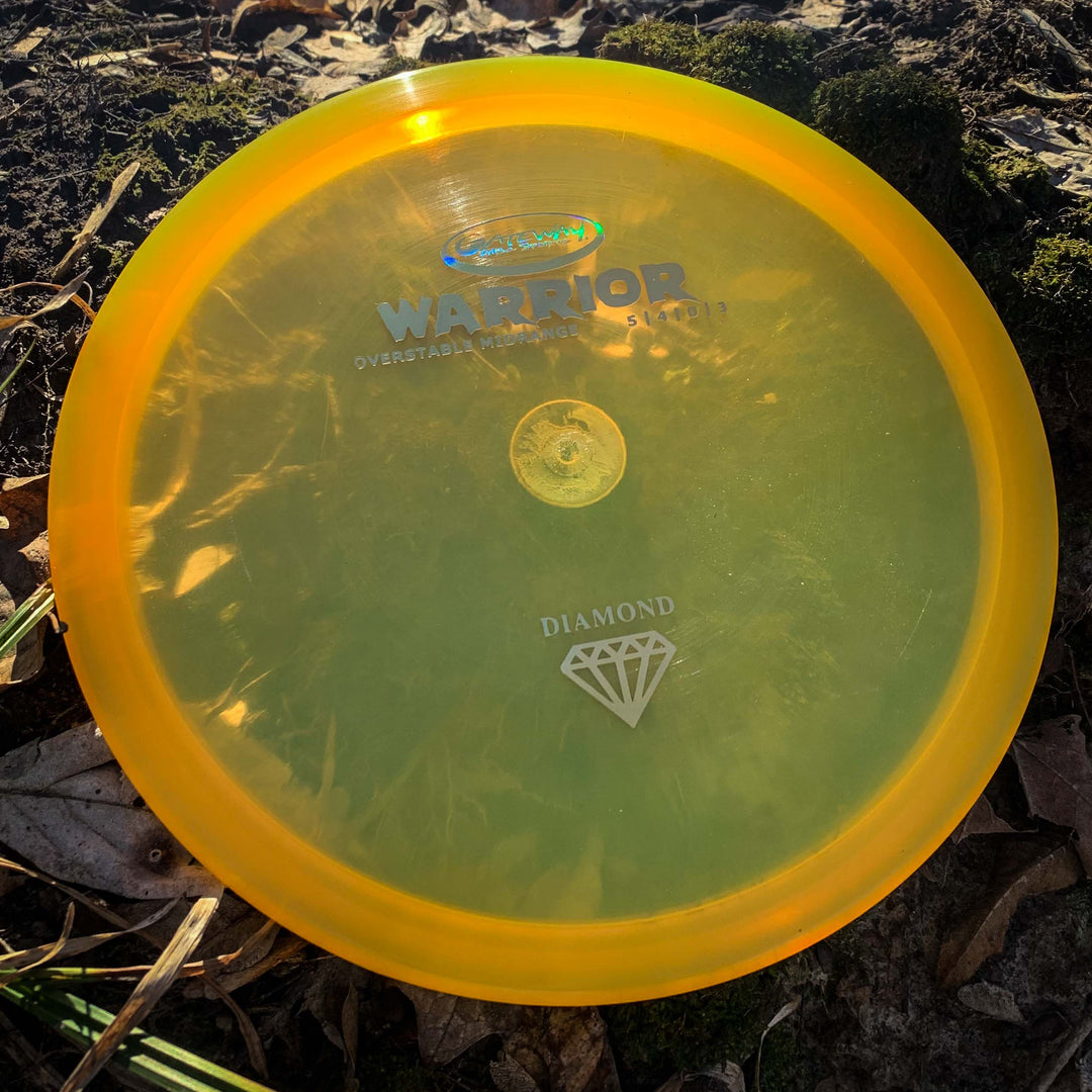 A Warrior - Diamond yellow overstable mid-range disc lies on the ground among leaves and moss.